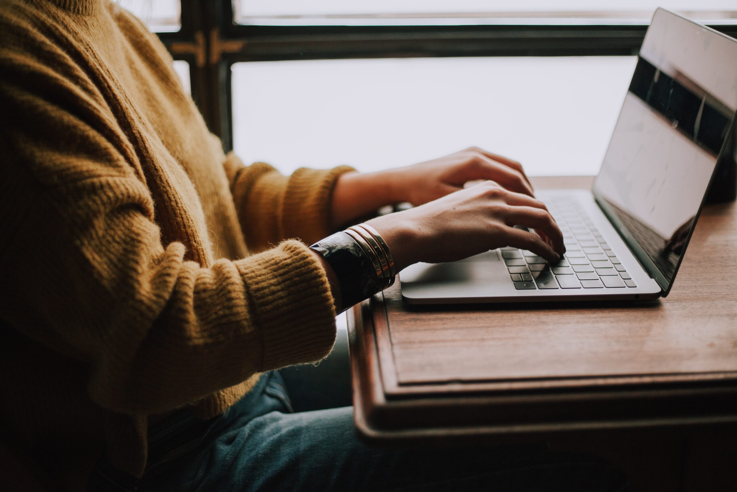 weiblich gelesene Person mit gelben Strickpulli arbeitet am Laptop