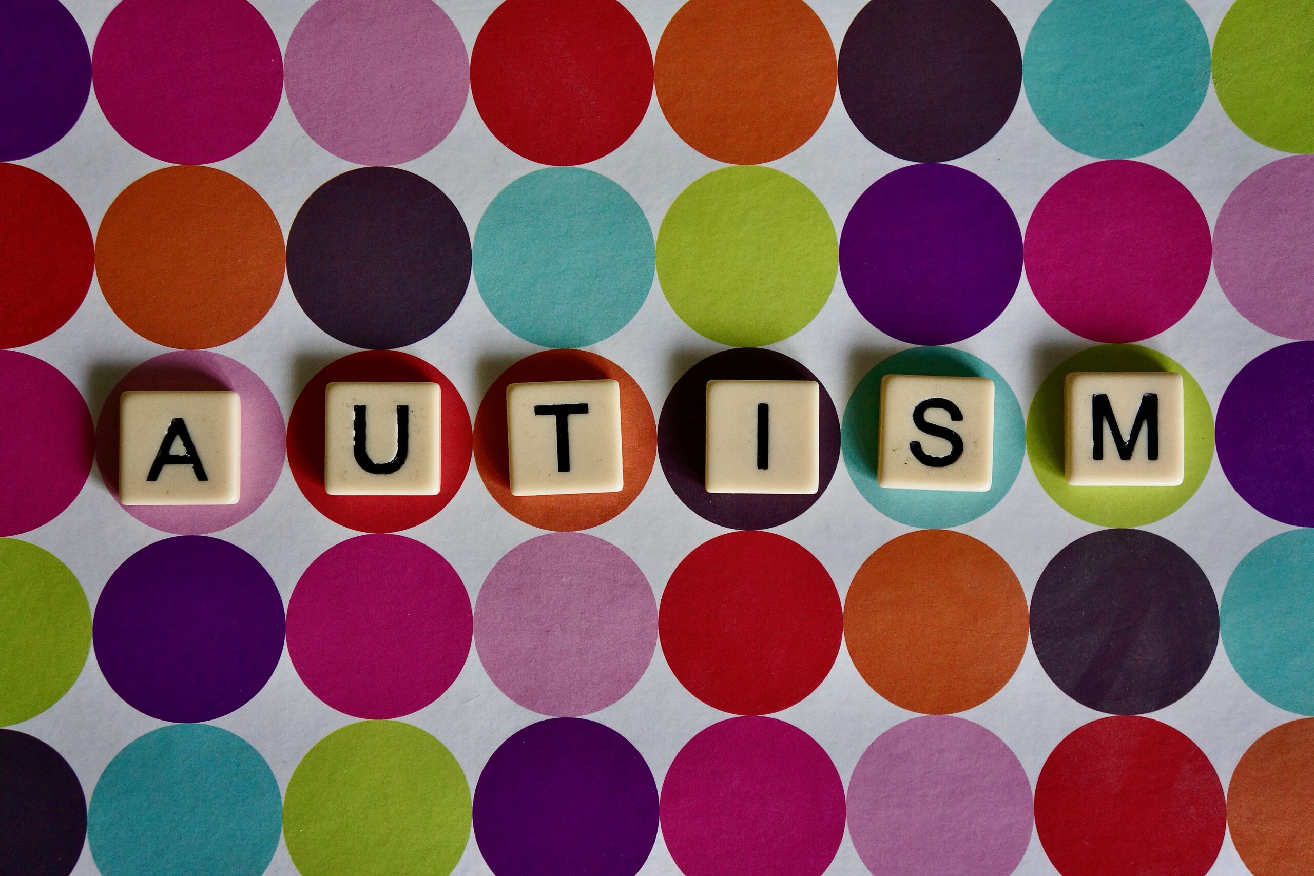 Auf einem grauen Hintergrund liegen Kreise in verschiednen Farben. In Scrabble-Buchstaben steht dort das Wort Autism