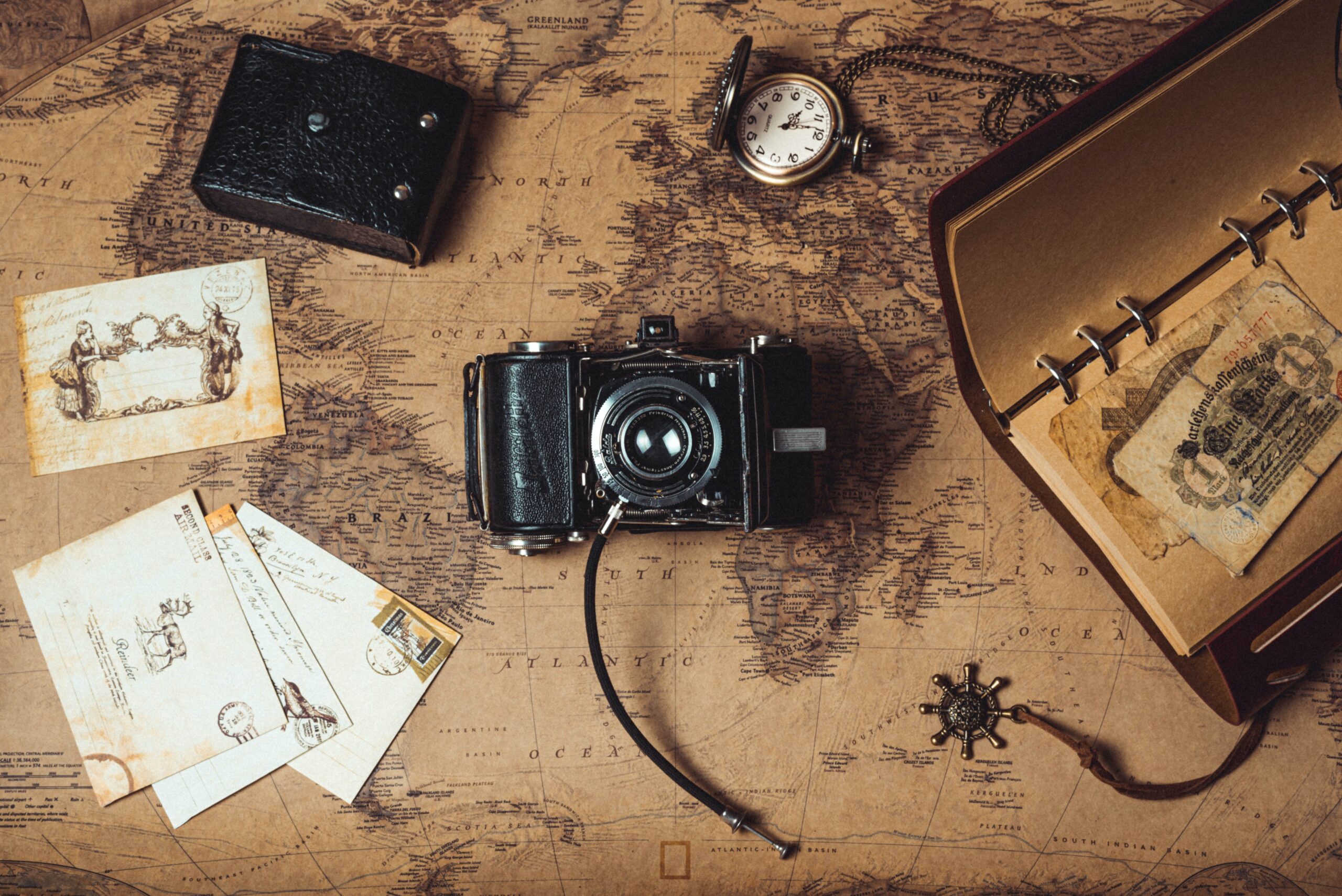 Eine Kamera liegt auf einer alten Karte. Daneben eine Taschenuhr und analoge Bilder.