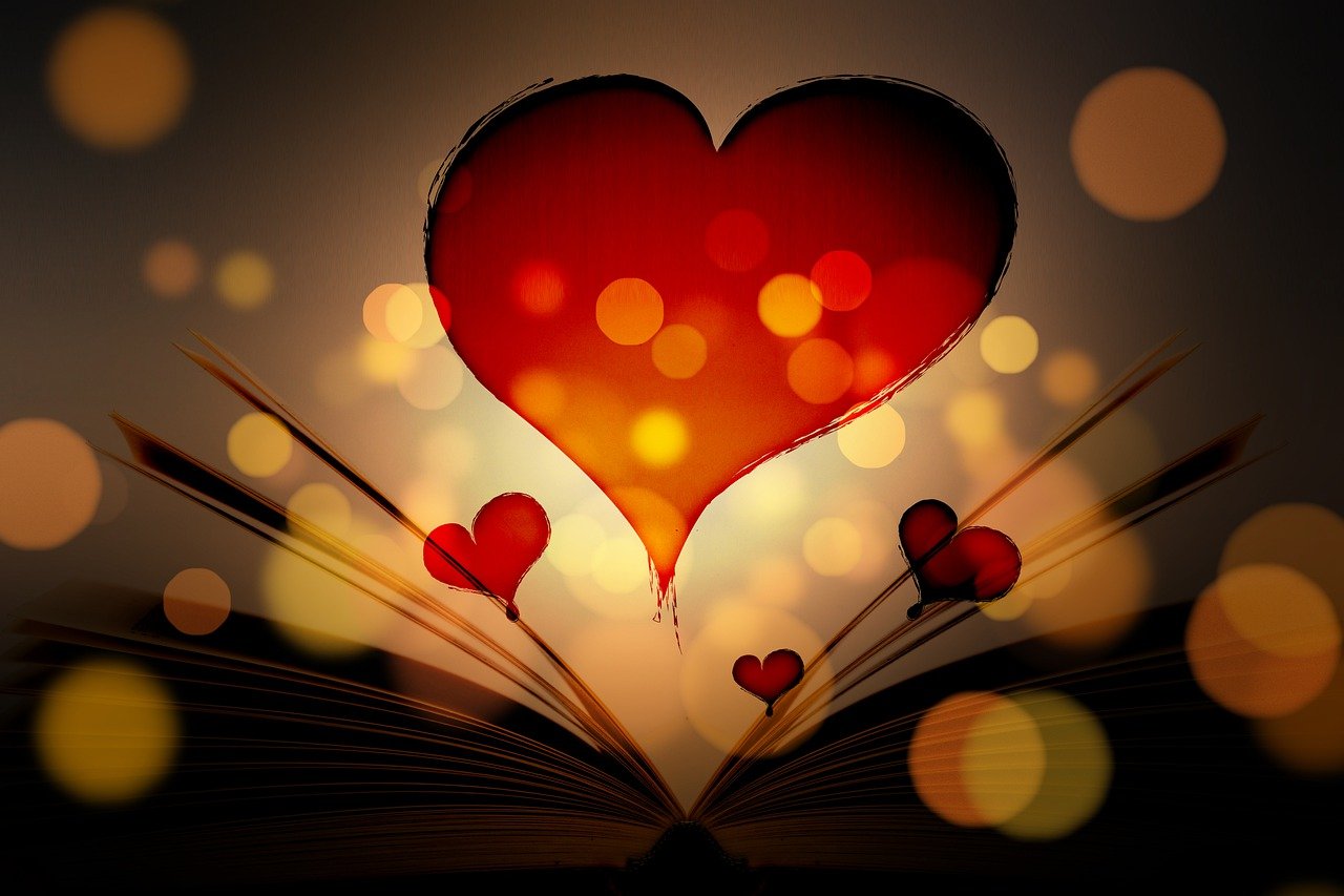Ein aufgeschlagenes Buch mit Seiten, die sich in der Mitte nach oben wölben und ein großes Herz in der Mitte formen. Über dem Buch schweben drei kleinere Herzen, die wie Ballons aussehen. Der Hintergrund ist dunkel mit vielen unscharfen Lichtpunkten, die eine warme, gemütliche Atmosphäre erzeugen.