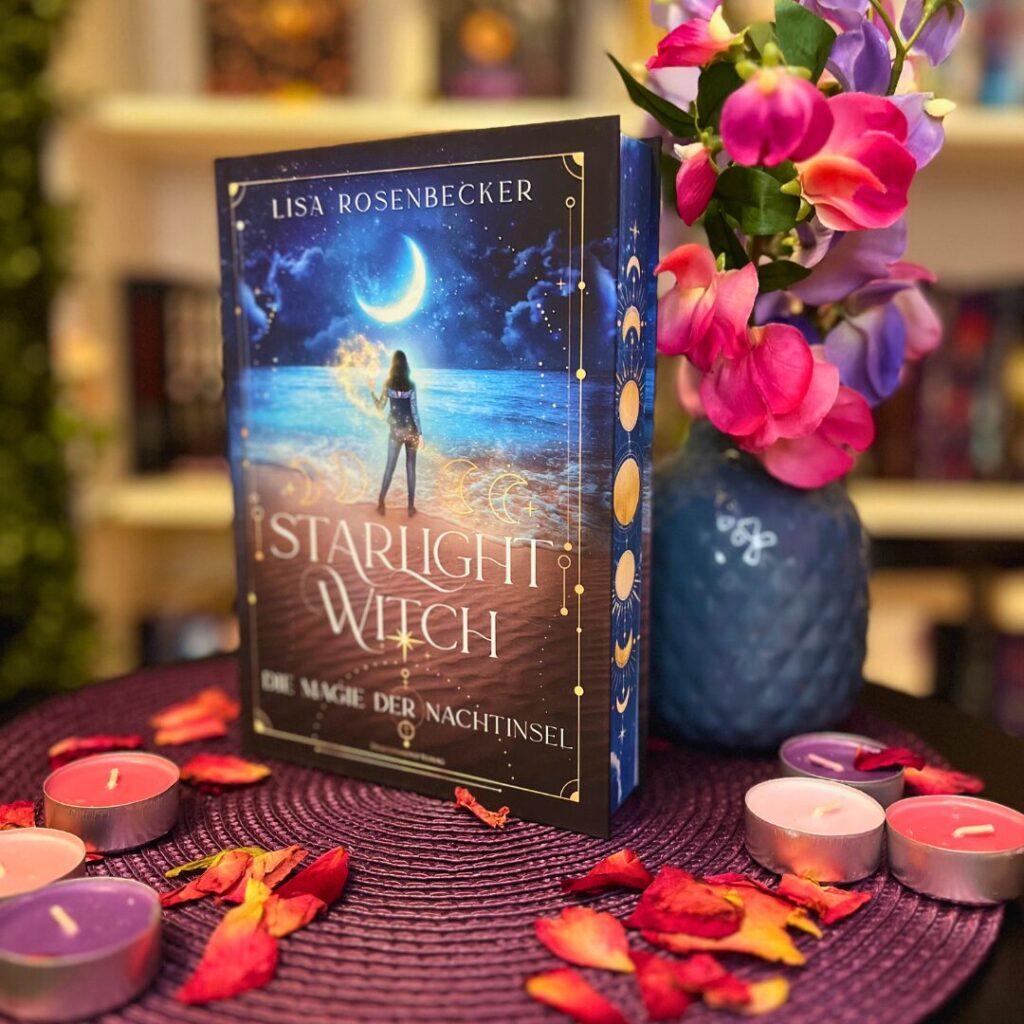 Das Bild zeigt ein Buch mit dem Titel "Starlight Witch: Die Magie der Nachtinsel" von Lisa Rosenbecker. Das Buch steht aufrecht auf einem runden, lila Untersetzer, der auf einem Tisch liegt. Um das Buch herum liegen einige getrocknete Rosenblätter und mehrere kleine Teelichter in verschiedenen Farben (lila, rosa, rot). Rechts neben dem Buch steht eine Vase mit einem blauen Muster, die mit rosa und lila Blumen gefüllt ist. Im Hintergrund sind unscharf Bücherregale zu erkennen.