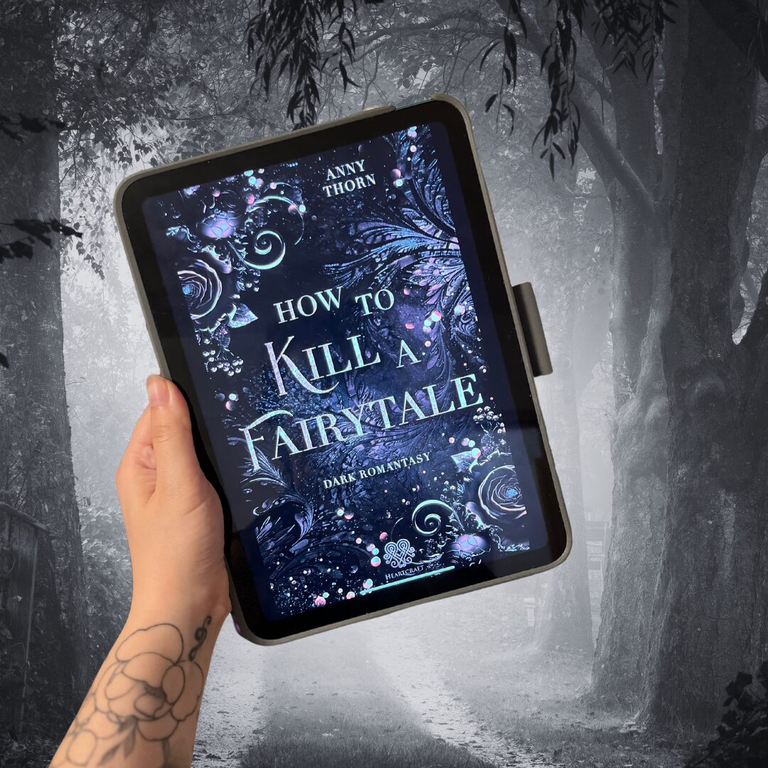 Das Bild zeigt eine Hand, die ein Tablet hält. Auf dem Bildschirm des Tablets ist das Cover eines Buches zu sehen. Der Titel des Buches lautet "How to Kill a Fairytale" und der Untertitel ist "Dark Romantasy". Der Autor des Buches ist Anny Thorn. Das Cover ist dunkel und zeigt verschnörkelte, mystische Muster und Blumen. Im Hintergrund des Bildes ist ein nebliger Waldweg zu sehen, der eine düstere und geheimnisvolle Atmosphäre vermittelt. Die Hand, die das Tablet hält, hat ein Tattoo eines Blumenmusters am Handgelenk.