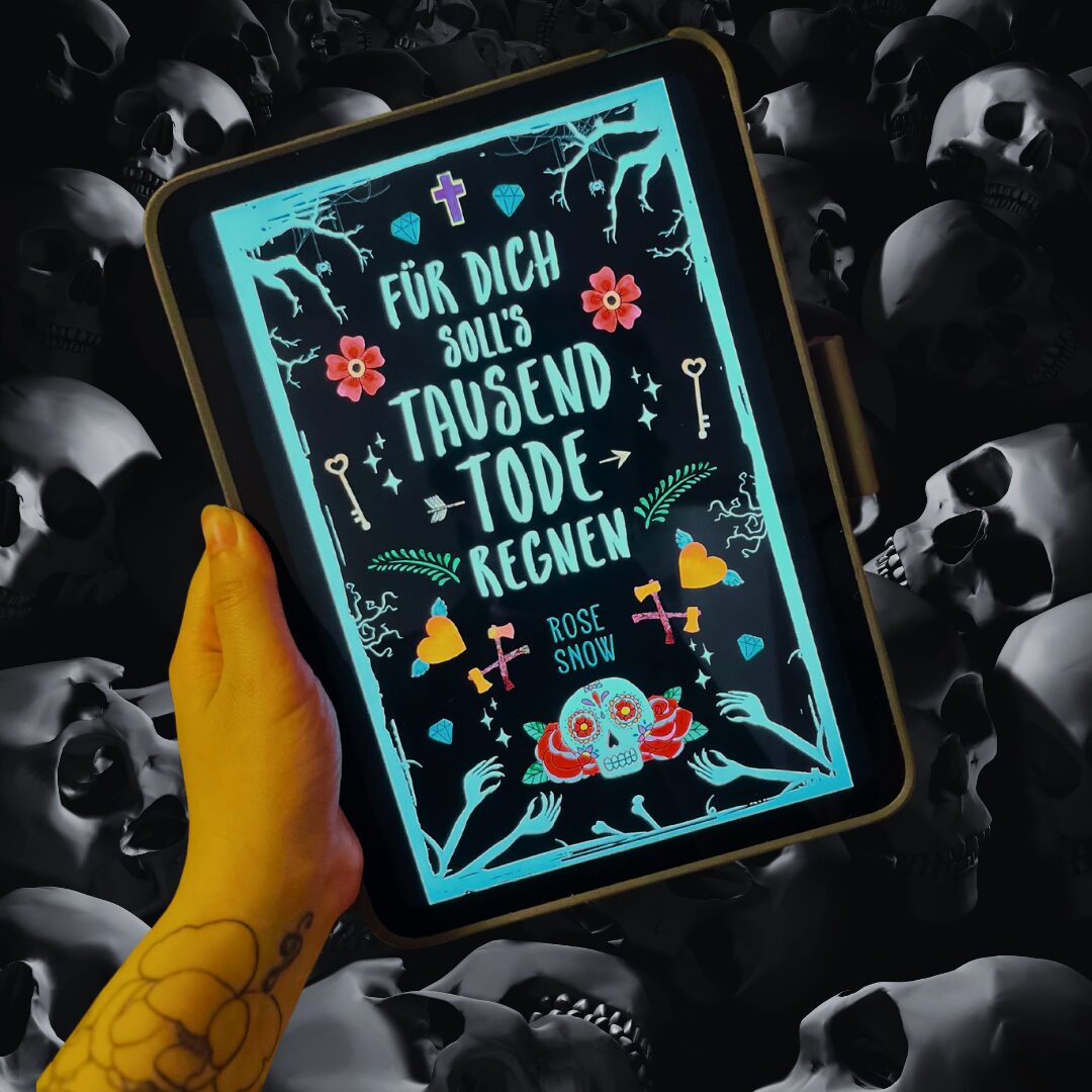 Das Bild zeigt eine Hand, die ein Tablet hält. Auf dem Bildschirm des Tablets ist das Cover eines Buches zu sehen. Der Titel des Buches lautet "Für dich soll's tausend Tode regnen" und der Autor ist Rose Snow. Das Cover ist dunkel mit hellblauen und bunten Verzierungen, darunter Blumen, Schlüssel, Herzen und ein Totenkopf mit Blumen. Im Hintergrund des Bildes sind viele Totenschädel zu sehen, die eine düstere Atmosphäre schaffen. Die Hand, die das Tablet hält, hat ein Tattoo auf dem Handgelenk.