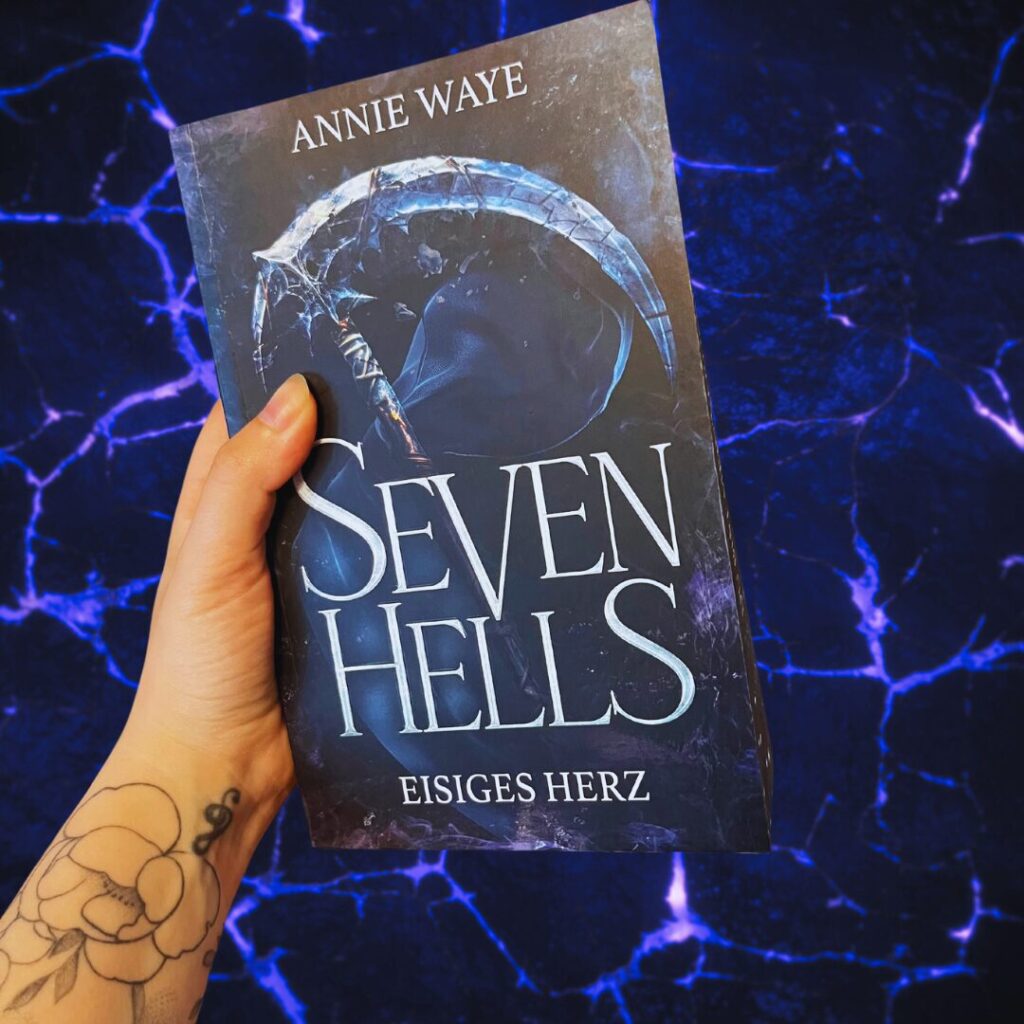 Das Bild zeigt eine Hand, die ein Buch hält. Der Titel des Buches lautet "Seven Hells: Eisiges Herz" und der Autor ist Annie Waye. Auf dem Buchcover ist eine große, eisige Sense abgebildet, die vor einem dunklen, mystischen Hintergrund zu sehen ist. Die Hand, die das Buch hält, hat ein Tattoo einer Blume auf dem Handgelenk. Der Hintergrund des Bildes ist dunkelblau mit leuchtenden, blitzartigen Linien.