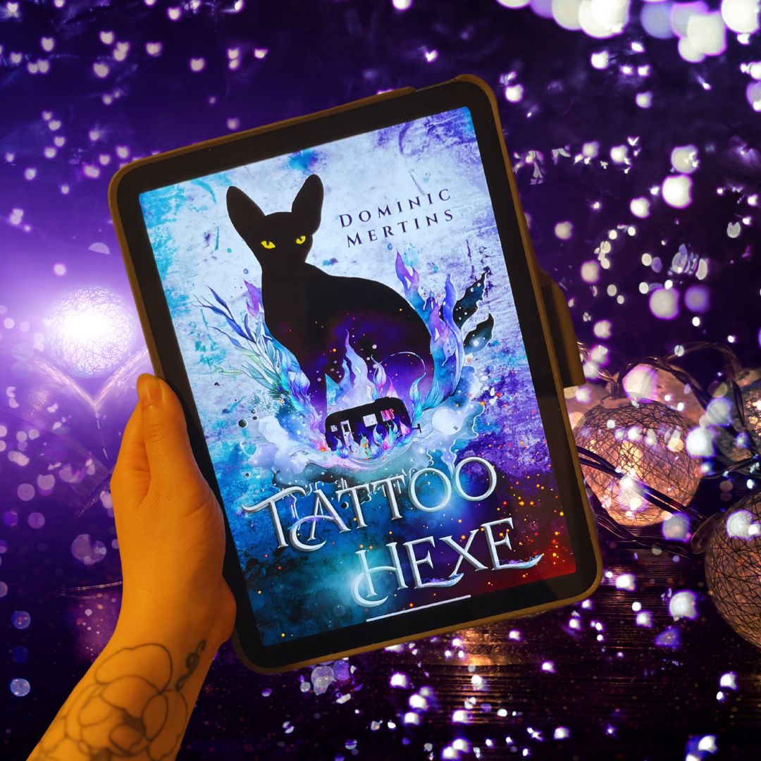 Das Bild zeigt eine Hand, die ein Tablet hält. Auf dem Bildschirm des Tablets ist das Cover eines Buches zu sehen. Das Buch heißt "Tattoo Hexe" und der Autor ist Dominic Mertins. Das Cover zeigt eine schwarze Katze mit gelben Augen, die vor einem Hintergrund aus blauen und violetten Flammen sitzt. Im Hintergrund sind auch mystische Symbole und ein Pentagramm zu sehen. Die Hand, die das Tablet hält, hat ein Tattoo von einer Blume auf dem Handgelenk. Der Hintergrund des gesamten Bildes ist dunkel und mit vielen kleinen, leuchtenden Lichtpunkten verziert, die eine magische Atmosphäre schaffen.