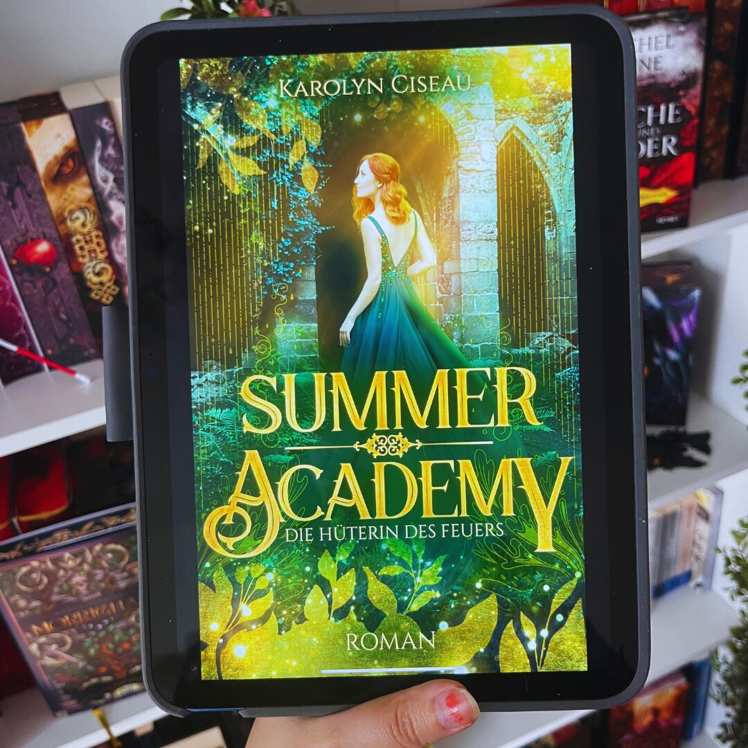 Das Bild zeigt ein Tablet, auf dem das Cover eines Buches angezeigt wird. Der Titel des Buches ist "Summer Academy: Die Hüterin des Feuers" von Karolyn Ciseau. Auf dem Cover ist eine Frau mit langen roten Haaren in einem eleganten, grünen Kleid abgebildet. Sie steht vor einem steinernen Torbogen, der von Pflanzen und leuchtenden Lichtern umgeben ist. Im Hintergrund sind Bäume und ein mystischer Wald zu sehen. Das Cover hat eine märchenhafte und magische Atmosphäre. Im Hintergrund des Bildes sind Bücherregale mit weiteren Büchern zu erkennen.