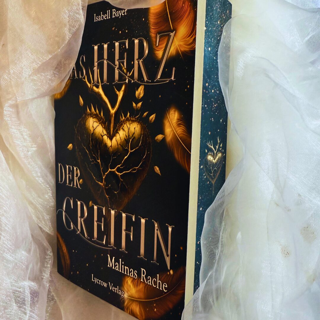 ein Buch mit dem Titel "Das Herz der Greifin: Malinas Rache" von Isabell Bayer. Auf dem Buchcover ist ein goldenes Herz mit Ästen und Blättern abgebildet, umgeben von goldenen Federn. Der Hintergrund ist dunkel gehalten, was das Herz und die Federn hervorhebt. Unten auf dem Cover steht "Lycrow Verlag". Das Buch ist in ein weißes, leicht transparentes Tuch eingewickelt.